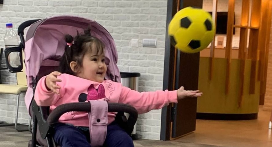 Девочка сидит в коляске и играет с мячом